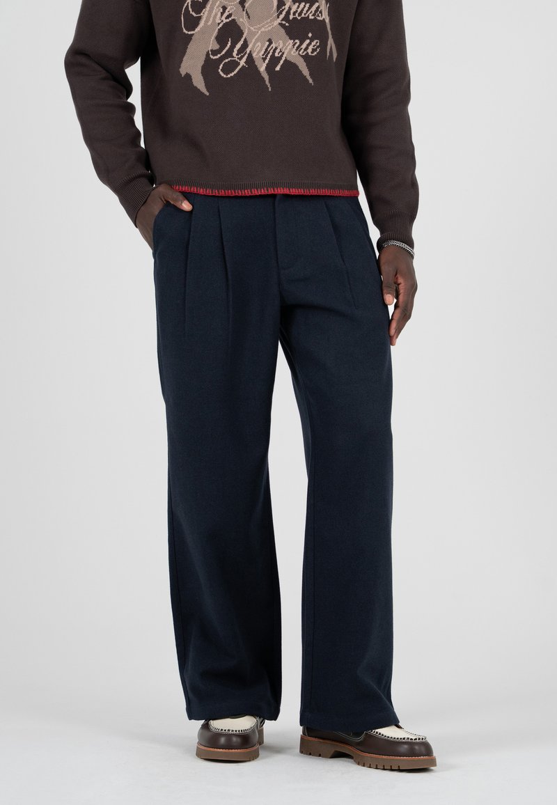 Pantalones de cuadros azul marino con un corte relajado, hechos de tela texturizada. Combinados con zapatos marrones que tienen una suela en contraste y costuras decorativas.
