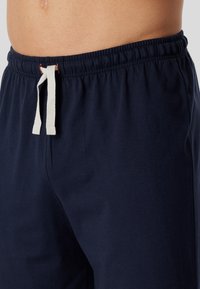 Navy blue cotton shorts with elastic waistband and white drawstring, featuring a smooth texture and side pockets.