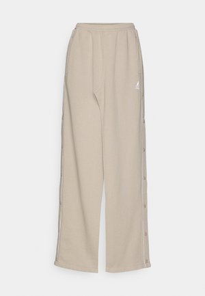 Pantaloni tuta beige realizzati in un tessuto morbido, con una vestibilità comoda, bottoni a scatto laterali e tasche frontali con un piccolo logo sull'anca.