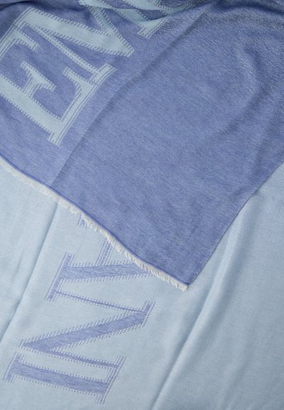 Tissu tissé bleu et bleu clair avec de grandes lettres en partie visibles et un bord frangé superposé au tissu plus clair.