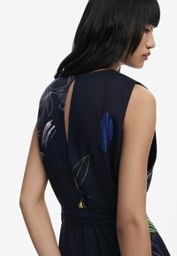 Floral-patterned dress in dark navy fabric, featuring a cut-out back, fitted waist, and thin belt accents in complementary colors.