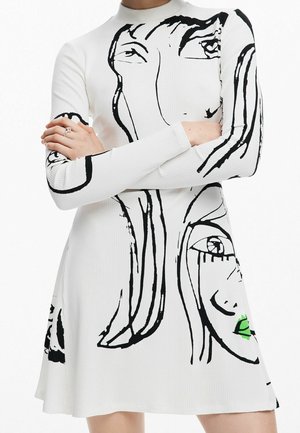 Biała prążkowana sukienka z czarnymi abstrakcyjnymi motywami twarzy, z zielonym akcentem na ustach jednej z twarzy. Długie rękawy i okrągły dekolt.