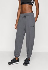 Sive trenirke z vrvico za prilagajanje v pasu in zoženimi manšetami; na levi nogi je logotip "adidas". Združene s črnimi športnimi čevlji.