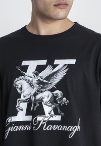 Černé bavlněné tričko s grafikou křídlatého koně a postavy v bílé barvě. Obsahuje výrazný design „K“ a značku „Gianni Kavanagh.“
