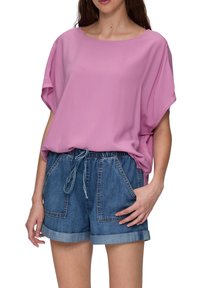 Roze, losvallend top met korte mouwen, gecombineerd met blauwe denim shorts met twee voorzakken en een trekkoord in de taille.