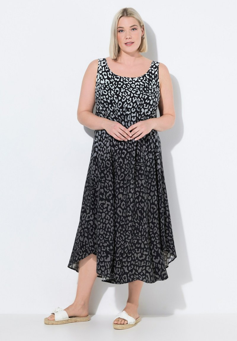 Schwarzes ärmelloses Kleid mit einem grauen Leopardenmuster, A-Linie-Form, fließender Stoff, knielanger Saum, kombiniert mit weißen Sandalen mit einer Schleifenverzierung.