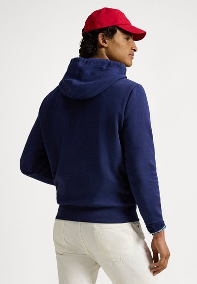 Μπλε σκούρο φούτερ με κουκούλα και μαλακή υφή, με κορδόνι στην κουκούλα και ριμπ σε τελείωμα, συνδυασμένο με τζιν ανοιχτόχρωμο. Κόκκινο καπέλο ως αξεσουάρ.