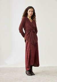 Top burdeos con mangas largas y detalle de lazo, combinado con una falda estampada a juego. Botines marrones completan el conjunto.