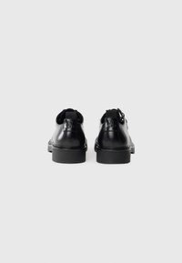 Zapatos de cuero negro con un acabado brillante, puntera redondeada, acentos texturizados, tacón ligeramente elevado y dos tiradores en la parte posterior para facilitar su calzado.