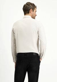 Camicia bianca a maniche lunghe con una texture liscia, taglio dritto e polsini con bottoni, abbinata a jeans neri con un classico design a cinque tasche.