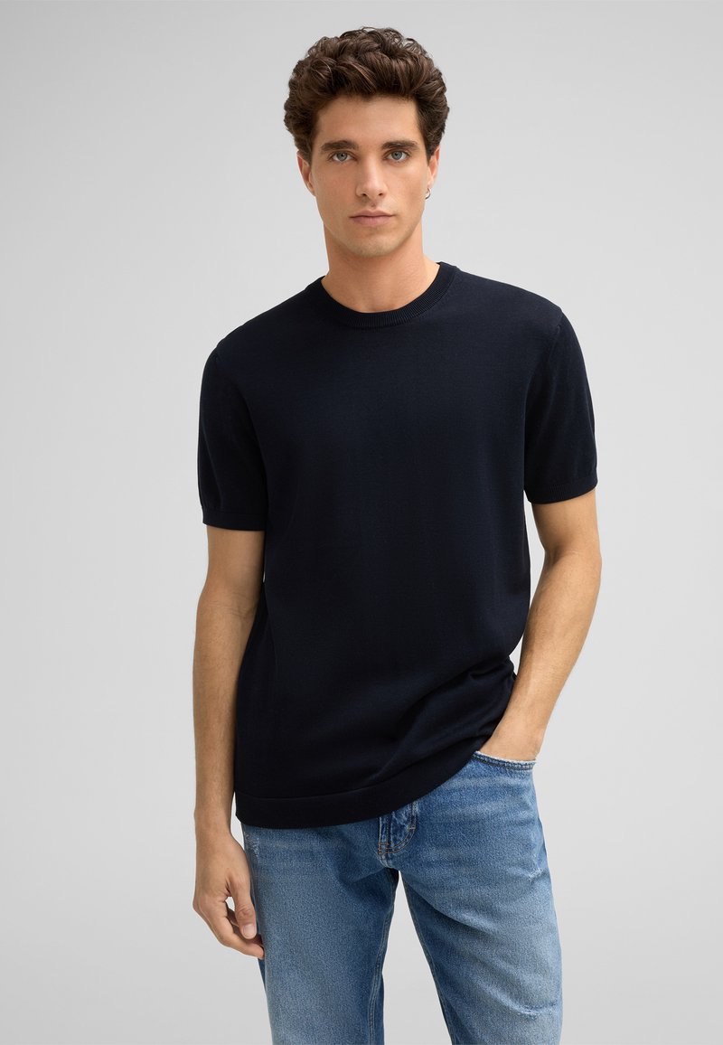Kurzärmeliger navyblauer Rundhalsausschnitt-Pullover aus einem weichen Strick, kombiniert mit hellblauen Denim-Jeans. Einfaches Design mit lockerer Passform.