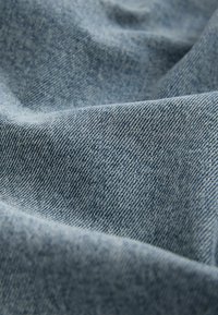 Țesătură din denim de un albastru deschis, cu o textură moale, având un țesut diagonal și variații subtile de culoare și umbrire.