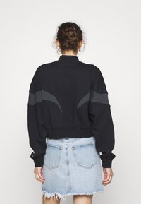 Svart kort sweatshirt med hög krage och grå accentpaneler; kombineras med en ljusblå jeanskjol med franskant och bakfickor.