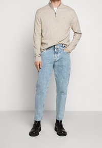 Suéter de punto beige con cuello de cremallera, combinado con jeans de pierna recta de color azul claro y botas de tobillo de cuero negro. Apariencia simple y casual.