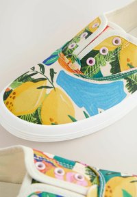 Lniane buty wsuwane z kolorowym wzorem z cytryn i tropikalnych liści, białą podeszwą i różowymi przelotkami, widoczne z ukośnego widoku z góry.