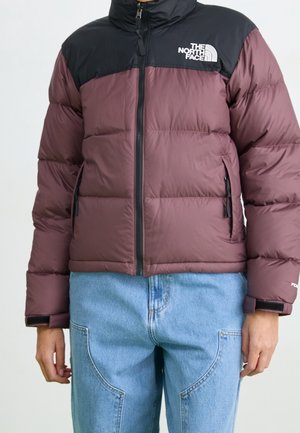 Viininpunainen ja musta North Face -toppatakki, jossa edessä vetoketju ja vetoketjulliset sivutaskut, yhdistetty vaaleansinisiin farkkuihin.