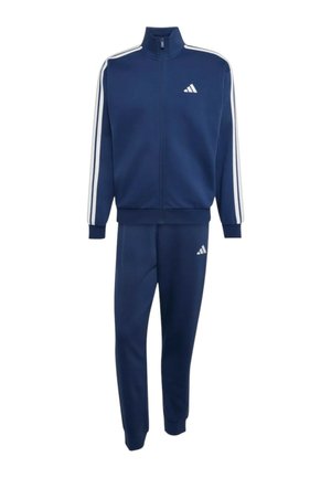 Temno modra trenirka z belimi stranskimi črtami na rokavih in hlačah, z zadrgo spredaj in belimi Adidas logotipi na prsih in nogi.