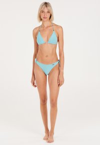 Turkusowy bikini z trójkątnym stanikiem z regulowanymi ramiączkami oraz dołem z wiązaniem po bokach, wykonane z miękkiej, teksturowanej tkaniny.