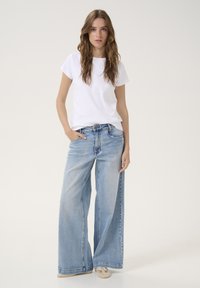 T-shirt bianco in cotone abbinato a jeans in denim a gamba larga di un blu chiaro. I jeans presentano un design classico a cinque tasche e un lavaggio chiaro.
