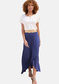 Top bianco a maniche corte abbinato a una lunga gonna fluente blu navy con un'alta scollatura, completato da una cintura intrecciata beige e sandali con punta aperta.