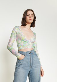 Top cropped de manga longa em cores pastel, com um design floral e abstrato, combinado com jeans de cintura alta.