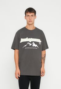 Camiseta gris de manga corta con gráfico de montaña en blanco y el logo "Jack & Jones". Tejido suave con un corte relajado; diseño minimalista.