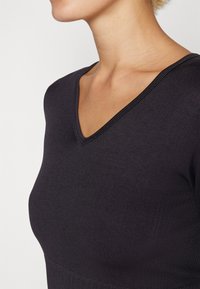 Black knit top with a V-neck, smooth texture, fitted silhouette, and ribbed detailing at the hem. Simple, classic design.