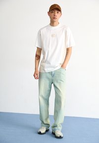 White t-shirt with logo and light blue loose jeans. Brown cap and beige sneakers with textured sole. Minimalist design and casual fit.