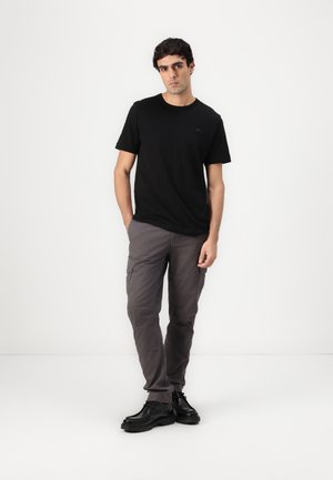 Schwarzes Baumwoll-T-Shirt mit kurzen Ärmeln, kombiniert mit grauen Cargo-Hosen mit Taschen und schwarzen Schnürschuhen, präsentiert auf einem schlichten Hintergrund.