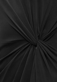 Μαύρο ύφασμα μαζεμένο και στριμμένο σφιχτά στο κέντρο, δημιουργώντας ακτινωτές πτυχώσεις και υφασμάτινο, ντυμένο μοτίβο.