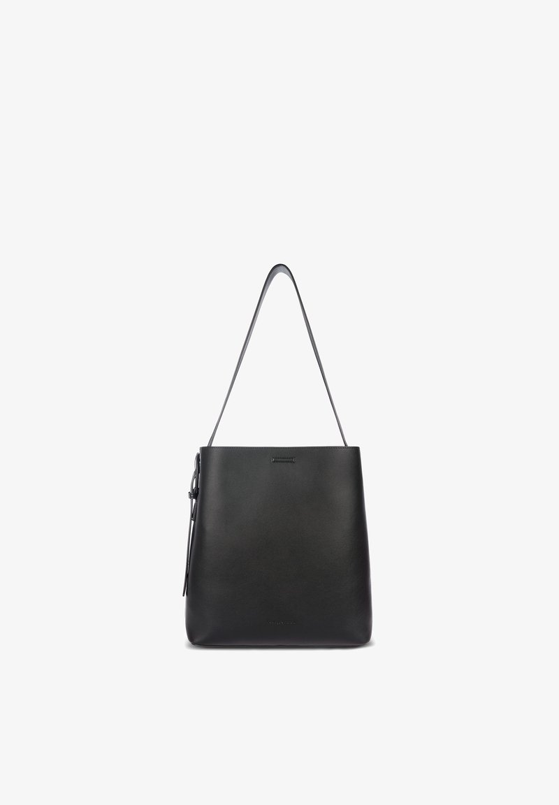 Sac à main en cuir noir avec une seule sangle d'épaule réglable et un design minimaliste, photographié sur un fond blanc.