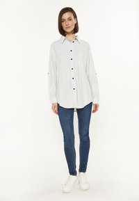 Camisa de manga larga a rayas con cuello, cierre de botones en la parte delantera y bolsillo en el pecho. Combinada con jeans skinny azules y zapatillas blancas.