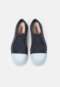 Scarpe in suede blu navy con punta in gomma bianca, design semplice con lacci e logo della soletta rossa a contrasto. Texture liscia in tutto il prodotto.