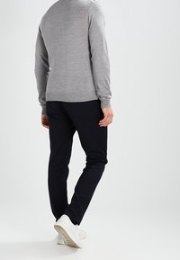 Pull gris clair à col rond, manches longues, associé à un pantalon bleu marine et des baskets blanches. Design simple et ajusté avec une texture lisse.