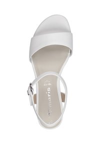 Vit sandal med en bred övre rem och en tunn ankelsrem med spänne, slät yta, platt sula och reflekterande logotyp inuti.