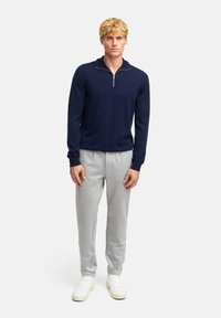 Maglione a maglia blu navy con zip a un quarto, abbinato a pantaloni jogger grigi chiari. Il maglione presenta un design aderente e polsini a costine.