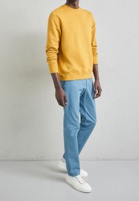 Sudadera de algodón amarilla con cuello redondo, combinada con pantalones ligeros azules y zapatillas blancas. Diseño simple sin patrones visibles.