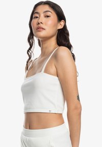 Hvid ribbet crop top med tynde stropper, der har en firkantet halsudskæring og en tætsiddende design, parret med matchende højtaljede underdele.