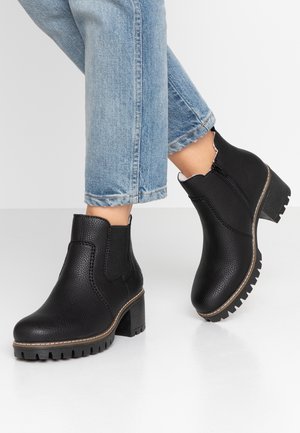 Botas negras hasta el tobillo con un acabado de cuero texturizado, cremallera lateral, punta redonda y un tacón grueso. Combinadas con jeans cortos azules.