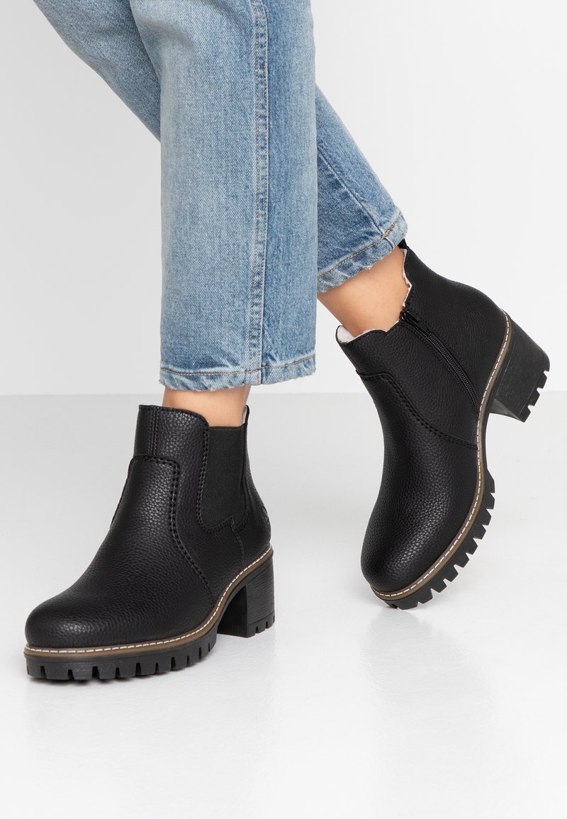 Botas negras hasta el tobillo con un acabado de cuero texturizado, cremallera lateral, punta redonda y un tacón grueso. Combinadas con jeans cortos azules.