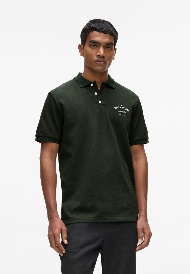 Polo vert foncé en tissu texturé, avec une patte de boutonnage à trois boutons et un logo brodé sur la poitrine gauche.