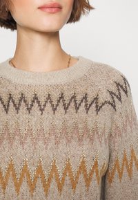 Sweter dzianinowy z okrągłym dekoltem, beżowy materiał z zygzakowymi wzorami w odcieniach brązu, różu i złota. Miękka tekstura i luźny krój.