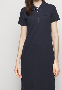 Námořnické polo šaty vyrobené z příjemného bavlněného materiálu se krátkými rukávy, zapínáním na knoflíky a kontrastním límcem. Obsahují malé značkové logo.