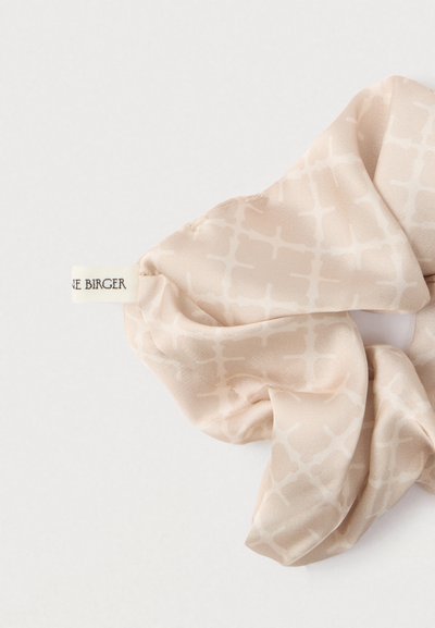 Coletero de satén beige claro con un sutil patrón de cuadrícula. Etiqueta adjunta con el texto "Birger" visible. Textura suave y forma delicada.