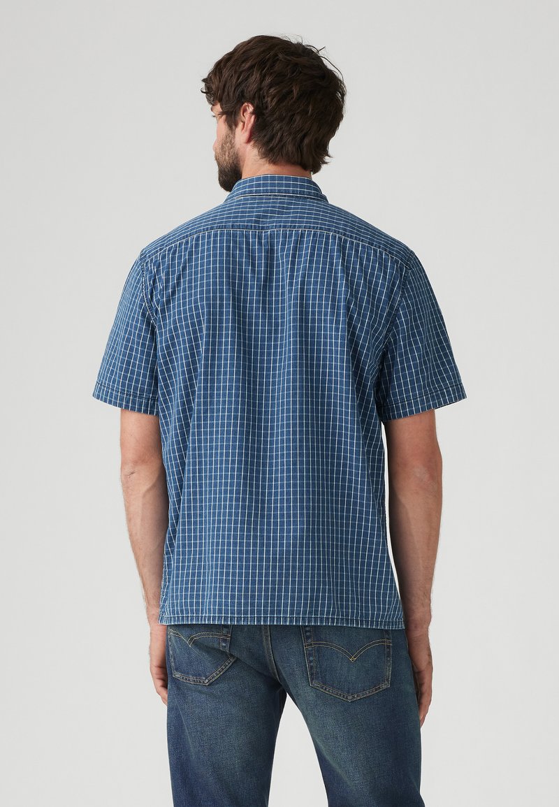 Camisa de manga corta en azul con un patrón de cuadritos. Fabricada con una tela de textura suave y con un cuello clásico. La vista trasera muestra detalles de costura.