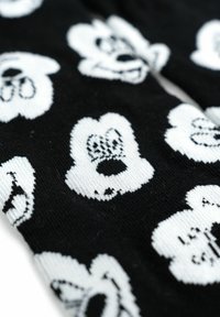 Tessuto nero con un motivo ripetitivo di volti di cartone animato bianchi con espressioni e caratteristiche distintive, lavorato a maglia in diverse trame.