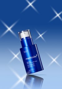 Bottiglia cilindrica blu con tappo a pompa trasparente. Etichetta con testo bianco. Base riflettente, sfondo scintillante. Capacità 30 ml.