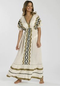 Vestido maxi de tela crema con patrones en zigzag en color oliva y negro. Cuenta con mangas abullonadas, escote en V y un dobladillo con volantes en capas. Textura suave.