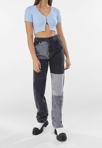 Top corto a costine blu chiaro con scollo a V e bottoni frontali. Pantaloni in denim a patchwork da grigio scuro a grigio chiaro e scarpe slip-on nere con suola spessa.
