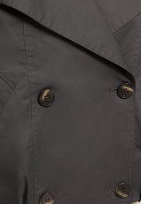 Temno sivi dvokraki plašč spredaj s štirimi temno rjavimi gumbi in vidnimi detajli šivov na gladki tkanini.